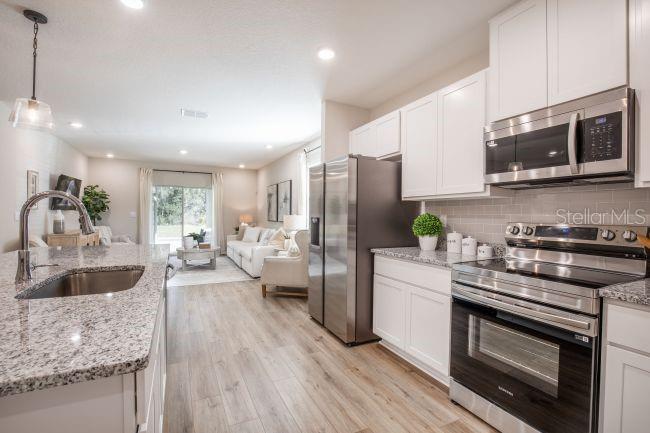 A kitchen with granite countertops and stainless steel appliances opens into a living room — 16815 NW 176TH TERRACE, ALACHUA, FL