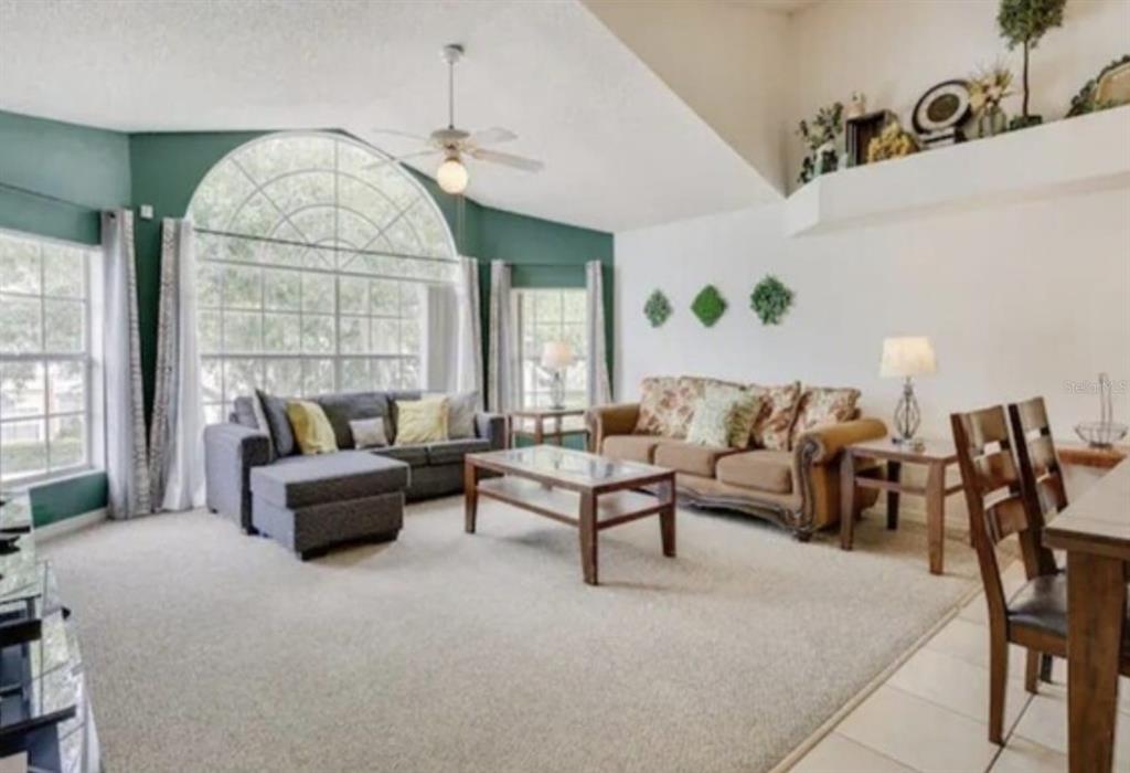 A living room with vaulted ceilings, a large arched window, and two sofas on carpet — 5004 LAGUNA BAY CIRCLE UNIT 54, KISSIMMEE, FL