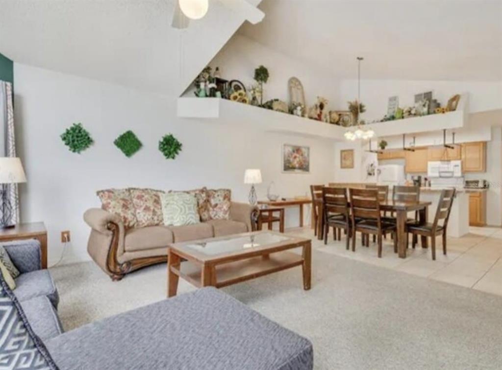 A living room with carpeted floors, a beige sofa, and an adjacent dining area — 5004 LAGUNA BAY CIRCLE UNIT 54, KISSIMMEE, FL