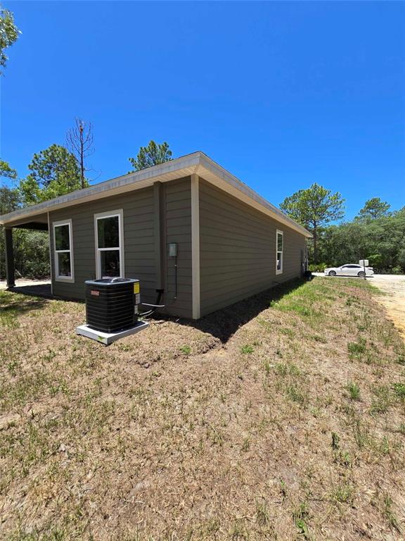 The exterior of a house features dark siding, a central air conditioning unit, and windows — 18082 PARAKEET ROAD, WEEKI WACHEE, FL