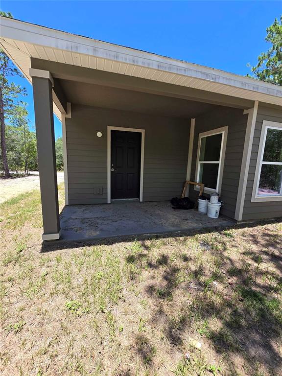 A covered porch with a dark door and two windows sits in front of a house — 18082 PARAKEET ROAD, WEEKI WACHEE, FL
