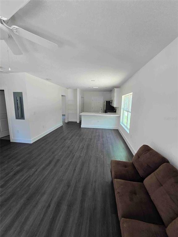 A living room with dark wood-look flooring leads to an open kitchen with white cabinets — 18082 PARAKEET ROAD, WEEKI WACHEE, FL
