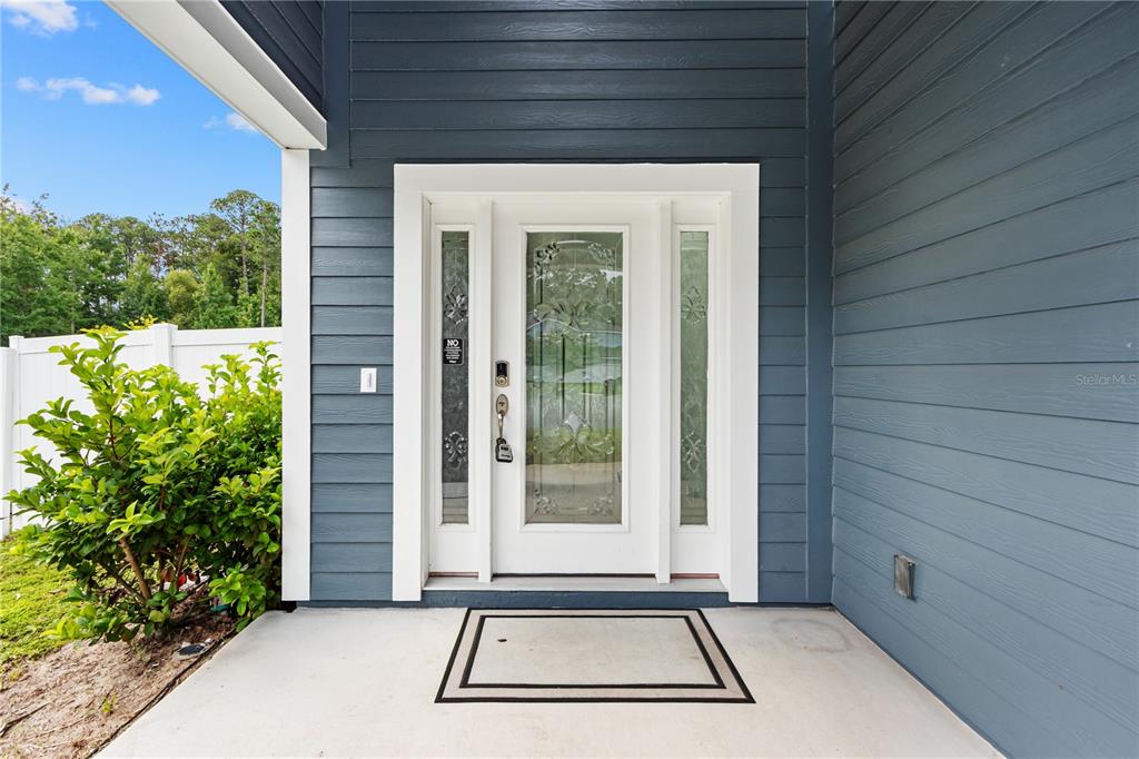 A white front door with glass panels is set against blue horizontal siding — 2004 HAWKEYE PLACE, FLEMING ISLAND, FL