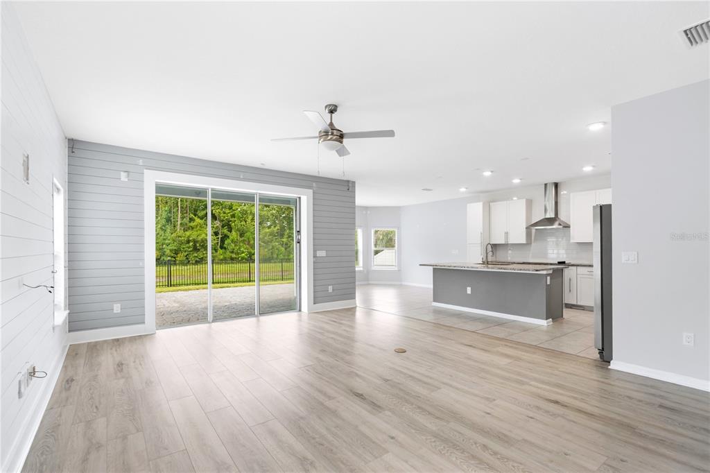 An open-concept living room and kitchen featuring light wood floors and gray shiplap accent walls — 2004 HAWKEYE PLACE, FLEMING ISLAND, FL