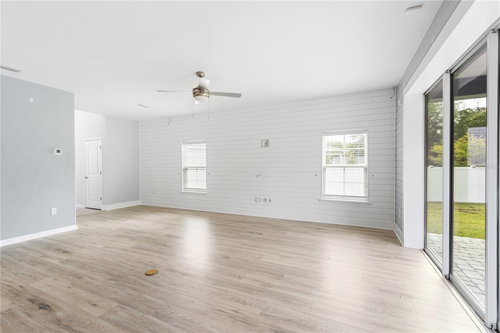 A bright living room features light wood-look flooring, white shiplap walls, and a sliding glass door — 2004 HAWKEYE PLACE, FLEMING ISLAND, FL