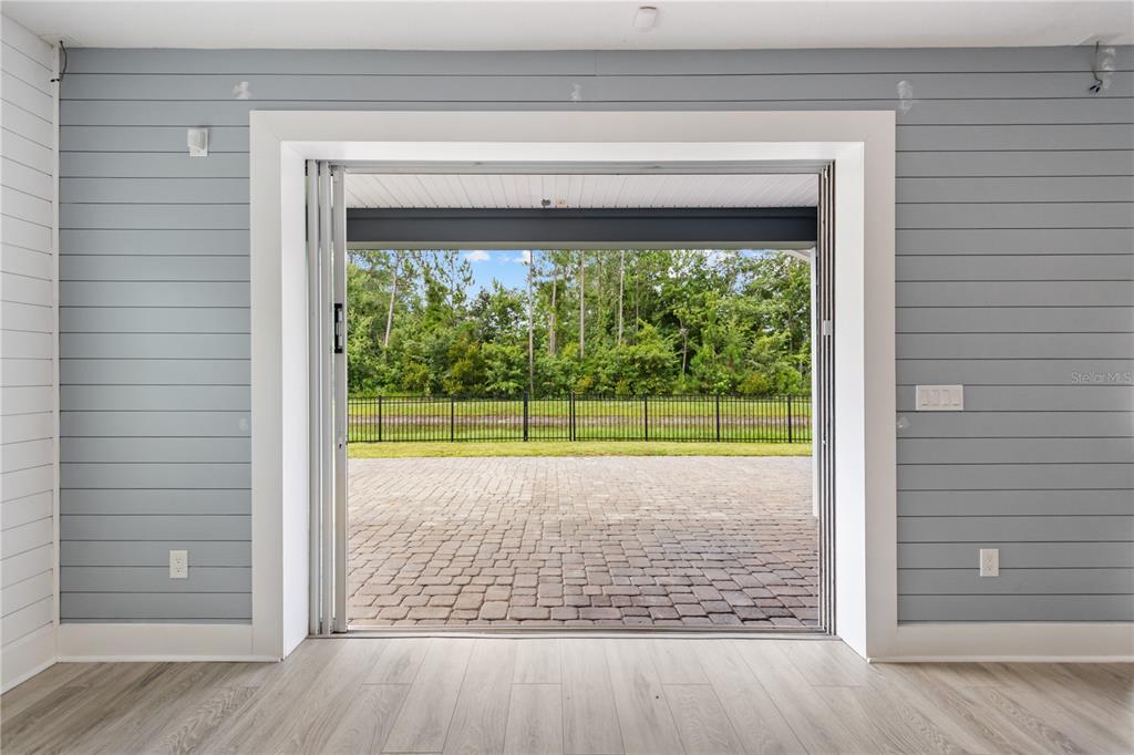 A room with light gray shiplap walls and wood-look flooring opens to a paved patio — 2004 HAWKEYE PLACE, FLEMING ISLAND, FL
