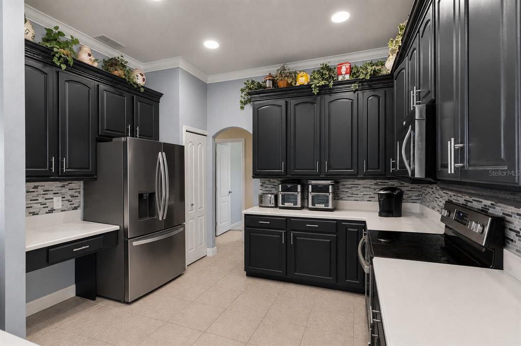 A kitchen with black cabinets, stainless steel appliances, white countertops, and a tiled backsplash — 631 WATERLAND COURT, ORLANDO, FL
