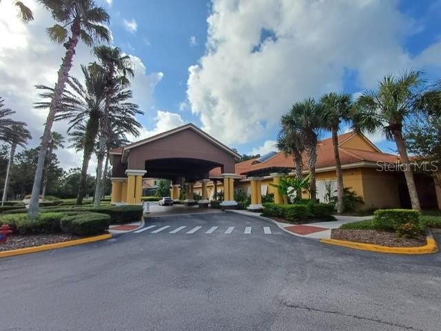 A large, yellow building with a covered entrance and palm trees under a cloudy sky — 3005 RED GINGER ROAD, KISSIMMEE, FL