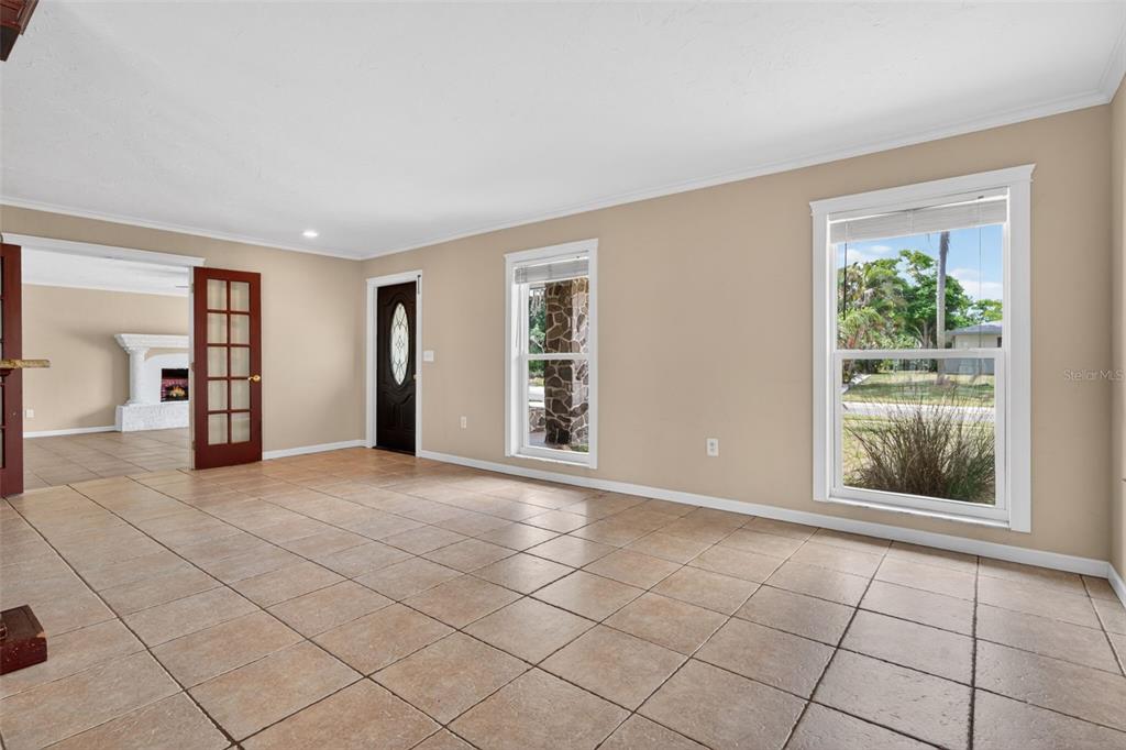 An empty room with tan tile flooring, beige walls, a front door, and two windows — 2555 CONSTITUTION BOULEVARD, SARASOTA, FL