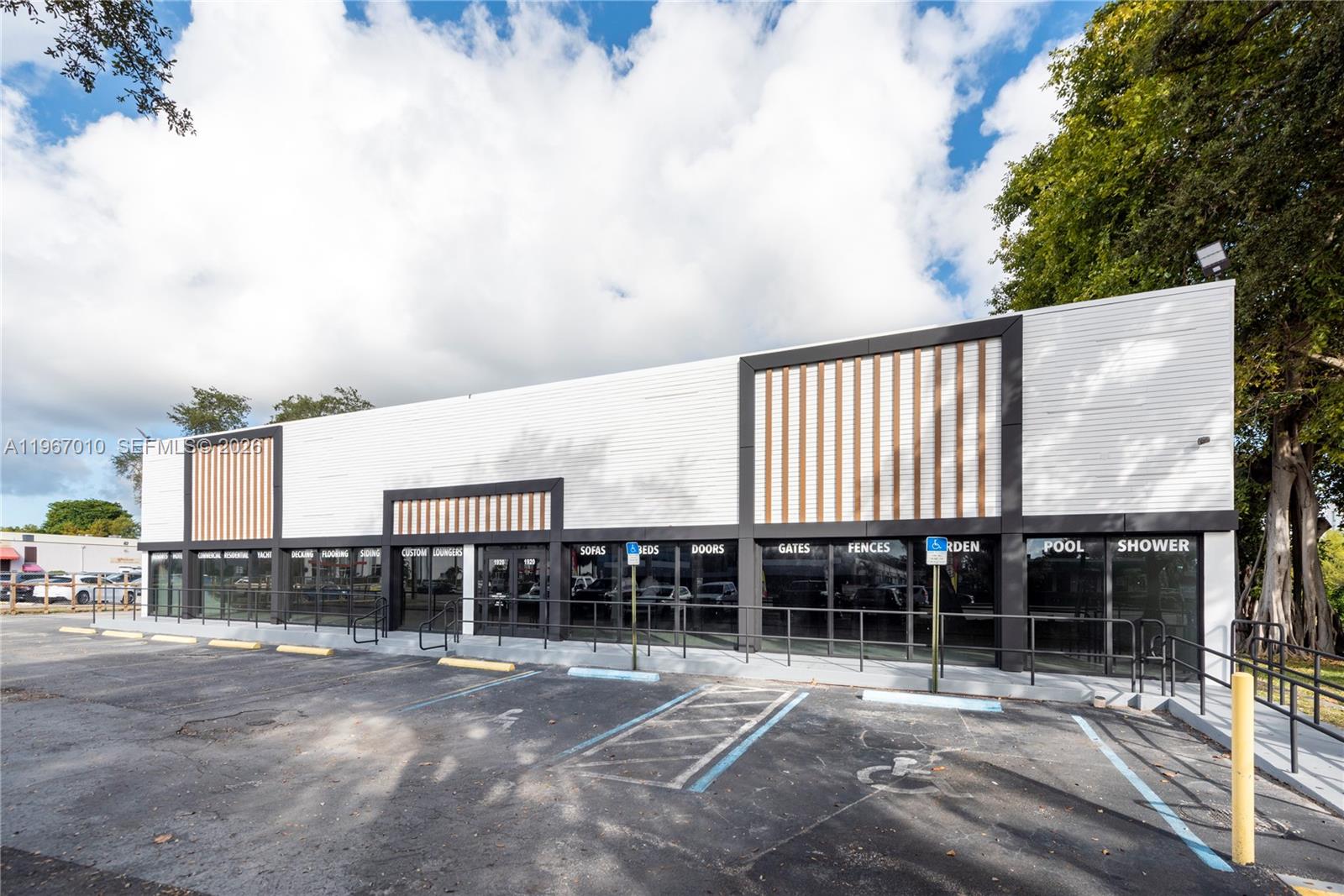 A commercial building exterior features white horizontal siding, dark trim, and large glass storefront windows — 1920-1936 Stirling Rd, Dania Beach FL 33004, DANIA BEACH, FL