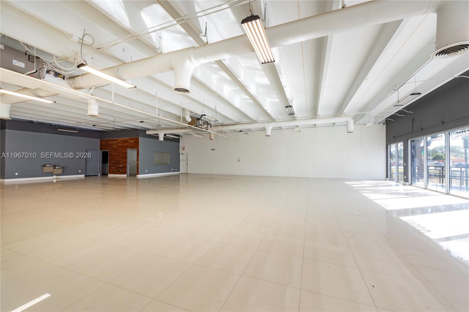 A large, open commercial space features white tiled floors, exposed ceiling beams, and glass storefront windows — 1920-1936 Stirling Rd, Dania Beach FL 33004, DANIA BEACH, FL