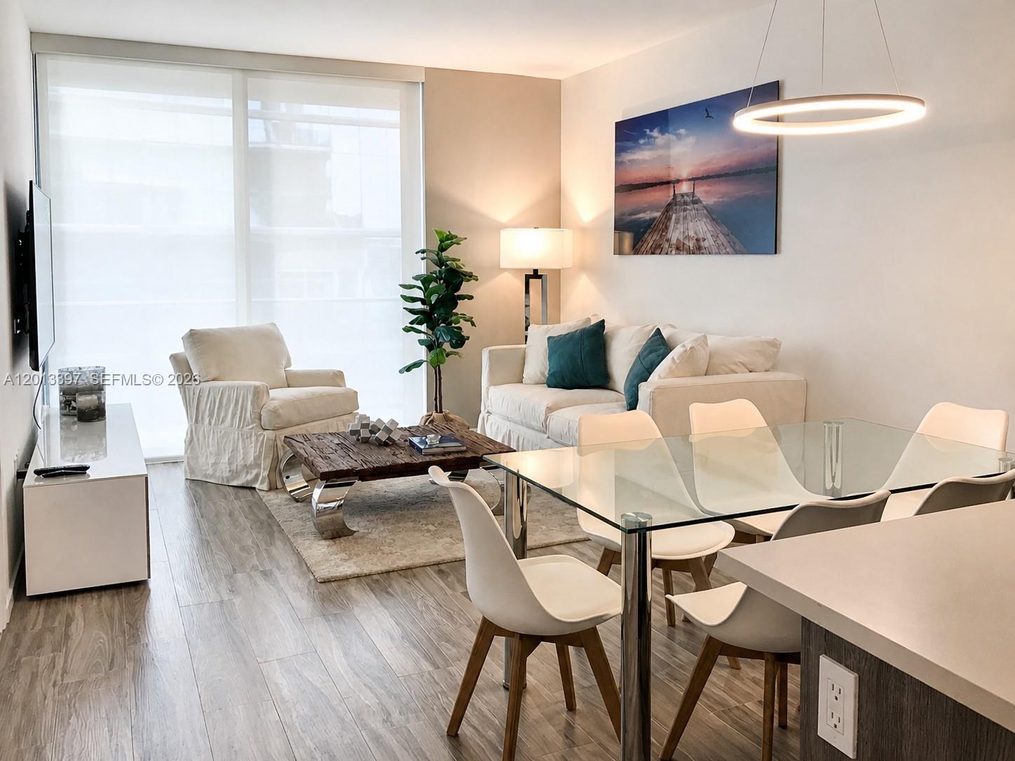 A modern living and dining area features a glass table, white sofa, and wood flooring — 801 S Miami Ave # 4206, Miami FL 33130, MIAMI, FL