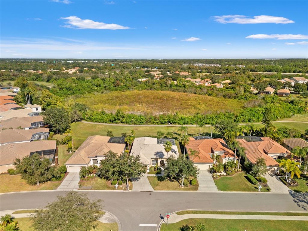 An aerial view shows a suburban street with houses, driveways, and a large grassy field — 6882 TAILFEATHER WAY, BRADENTON, FL
