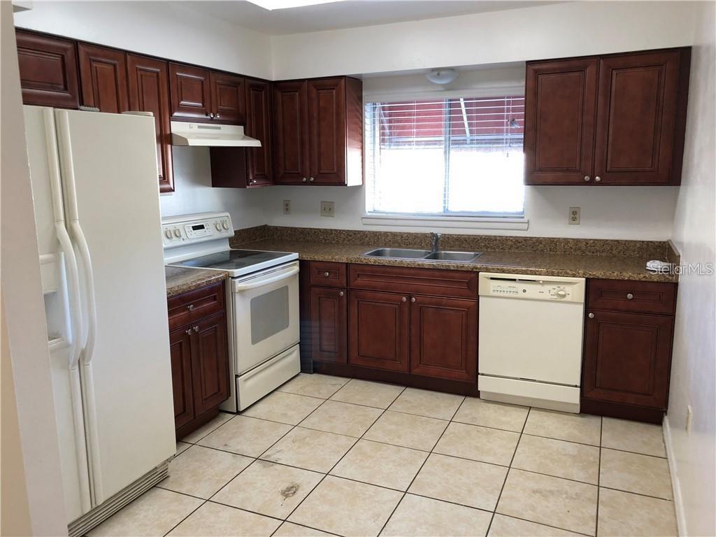 A kitchen features dark wood cabinets, granite countertops, white appliances, and light-colored floor tiles — 4213 S SEMORAN BOULEVARD UNIT 10, ORLANDO, FL