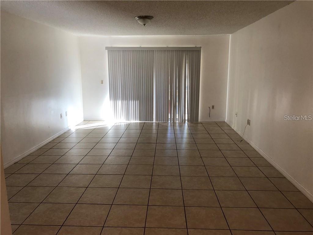 An empty room with beige tile flooring and vertical blinds covering a sliding glass door — 4213 S SEMORAN BOULEVARD UNIT 10, ORLANDO, FL