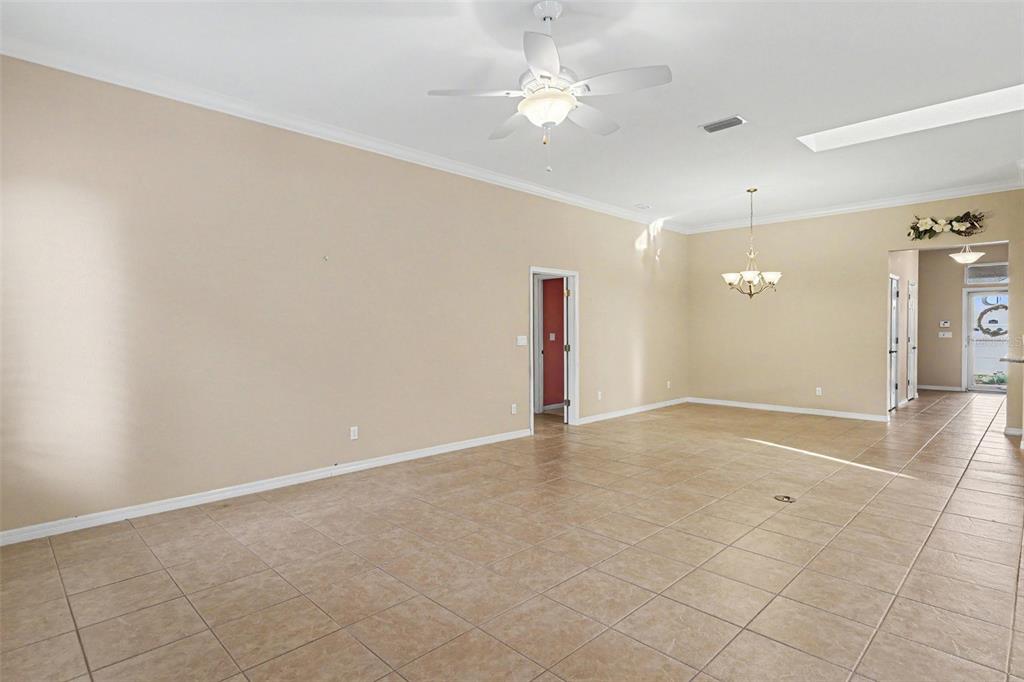 A spacious, empty room features beige walls, tiled flooring, a ceiling fan, and a chandelier — 10888 SE 170TH LANE ROAD, SUMMERFIELD, FL