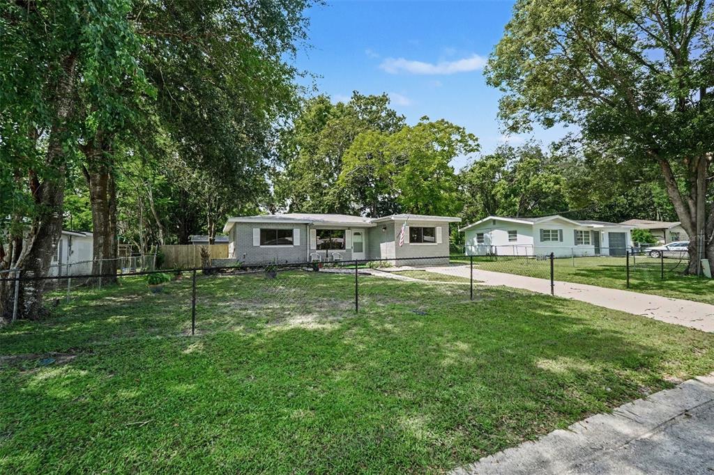 A single-story gray brick house with a chain-link fence and a concrete driveway — 21390 LEHOUIER DR, BROOKSVILLE, FL