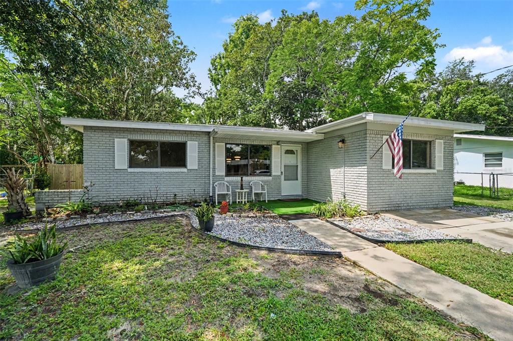 A single-story gray brick house with a front lawn, walkway, and an American flag — 21390 LEHOUIER DR, BROOKSVILLE, FL