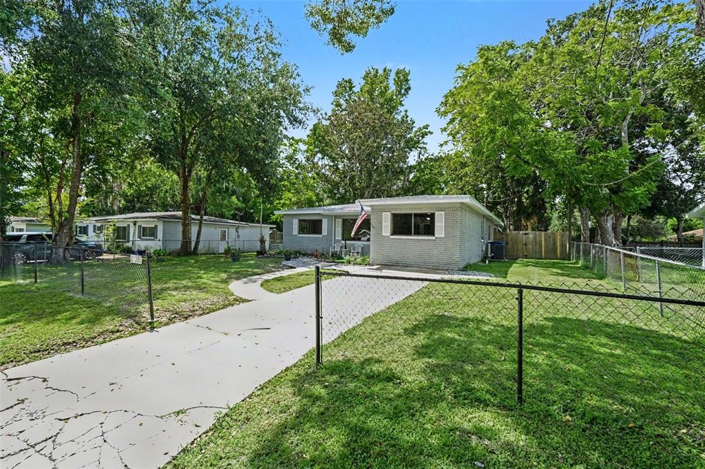 A single-story gray brick house with a concrete driveway and a chain-link fence — 21390 LEHOUIER DR, BROOKSVILLE, FL