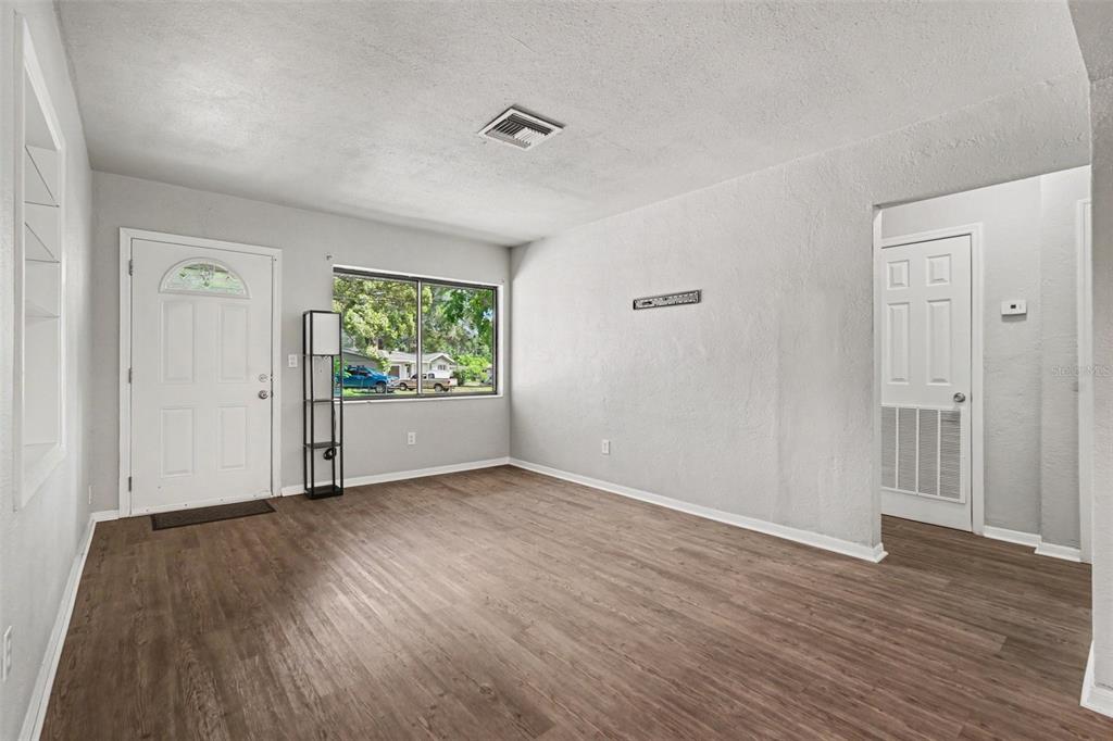 An empty living room features light gray walls, wood-look flooring, a front door, and a window — 21390 LEHOUIER DR, BROOKSVILLE, FL