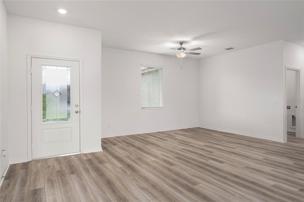 An empty room with white walls, wood-look flooring, a ceiling fan, and a front door — 404 MANITOBA LANE, POINCIANA, FL