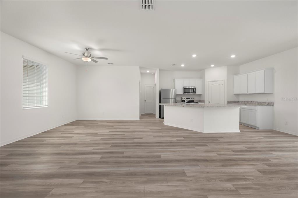 An open-concept living area features light wood-look flooring, a ceiling fan, and a white kitchen — 404 MANITOBA LANE, POINCIANA, FL