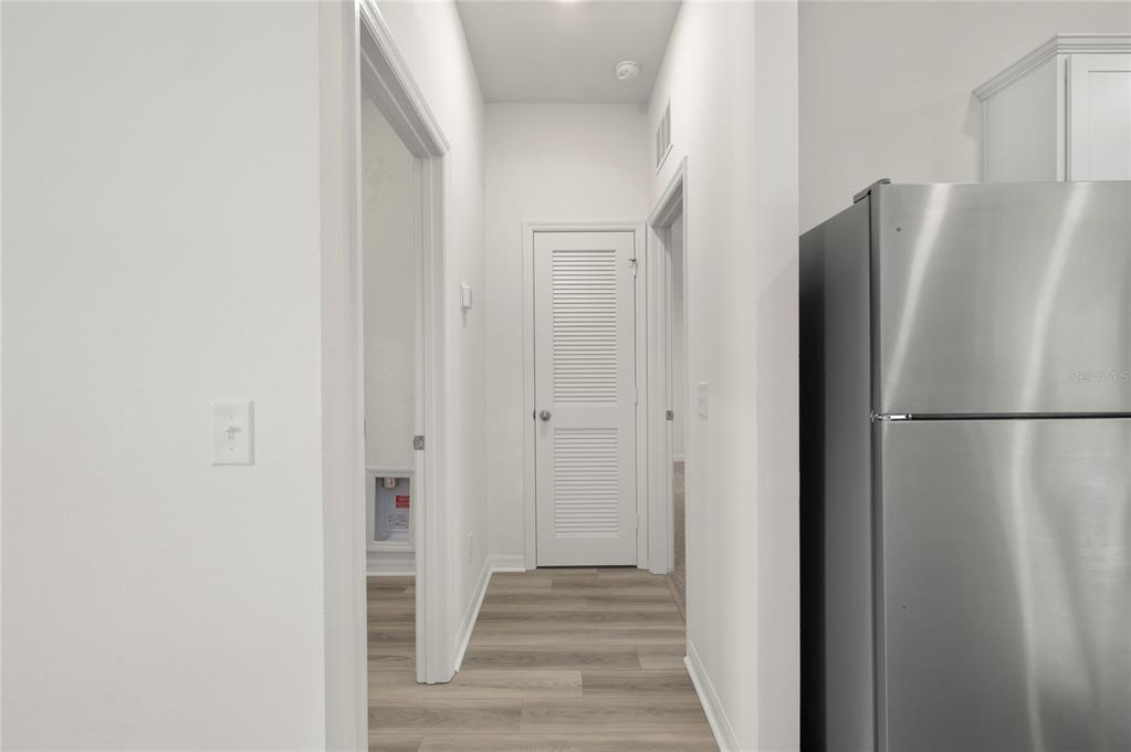A hallway with light wood-look flooring leads to a louvered door and a laundry area — 404 MANITOBA LANE, POINCIANA, FL