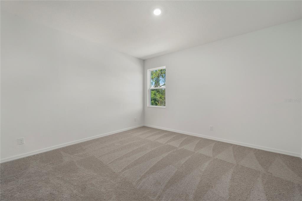 An empty bedroom features white walls, beige carpet, and a single window — 404 MANITOBA LANE, POINCIANA, FL