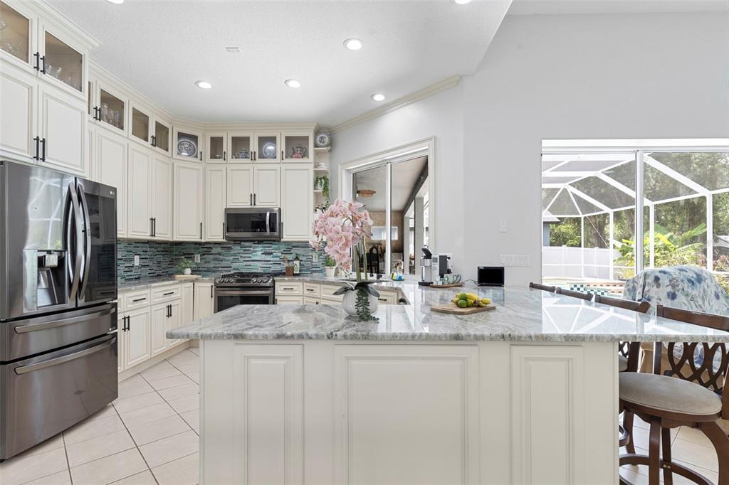 A kitchen features white cabinetry, granite countertops, a blue glass tile backsplash, and an island — 8380 GOLDEN PRAIRIE DRIVE, TAMPA, FL