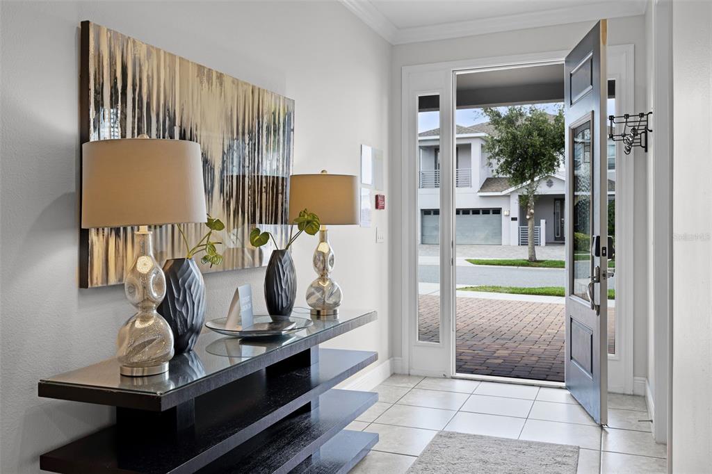 A modern entryway features a glass-topped console table, two lamps, and an open front door — 7739 GRABEN STREET, KISSIMMEE, FL
