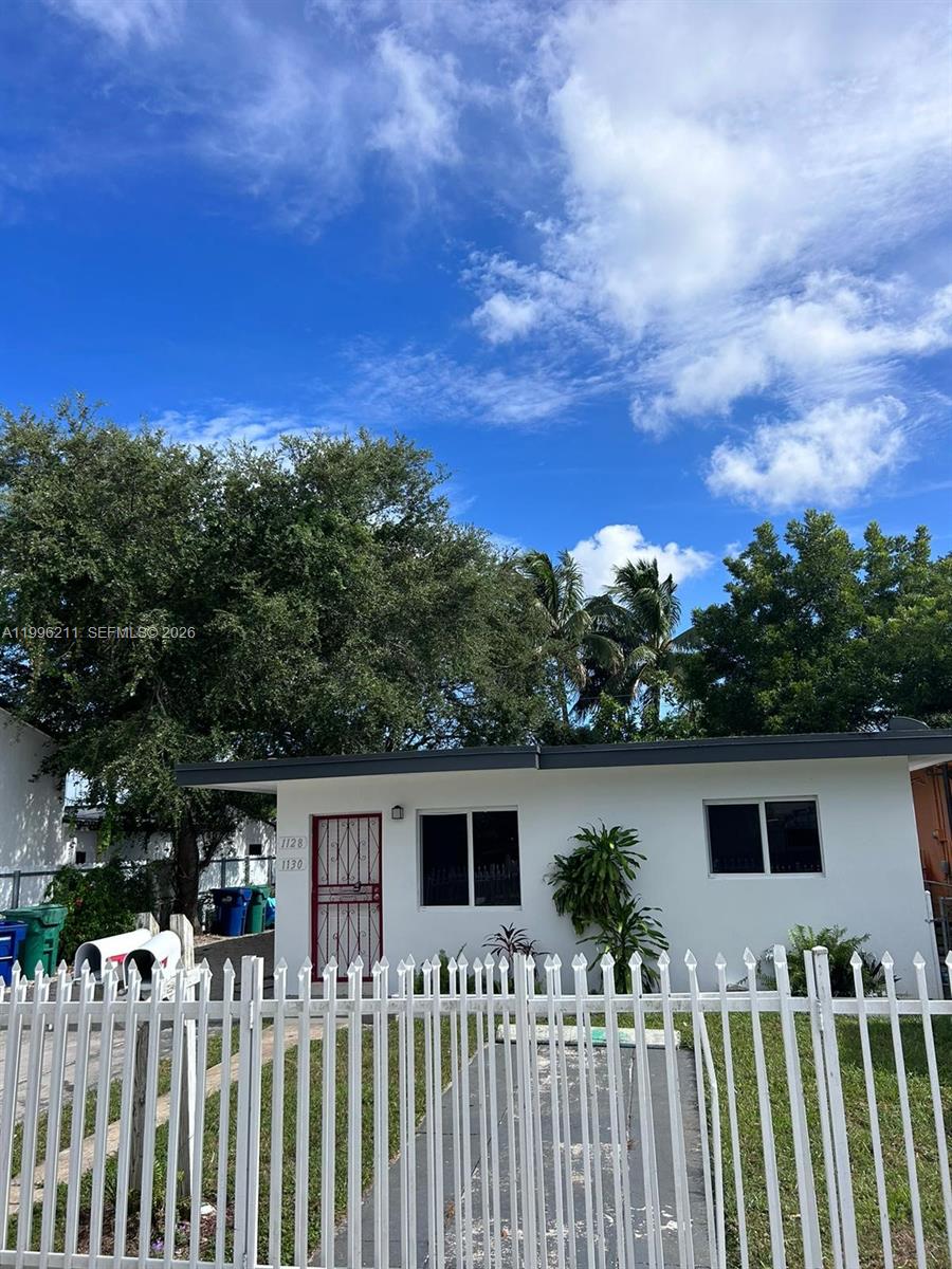 A single-story white house with a red security door sits behind a white metal fence — 1128 NW 76th St, Miami FL 33150, MIAMI, FL