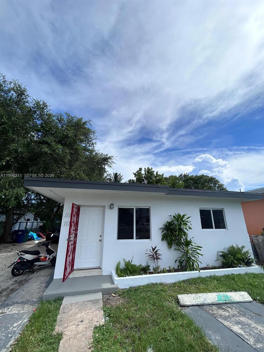 A white, single-story residential building features a red metal security door and a small garden — 1128 NW 76th St, Miami FL 33150, MIAMI, FL