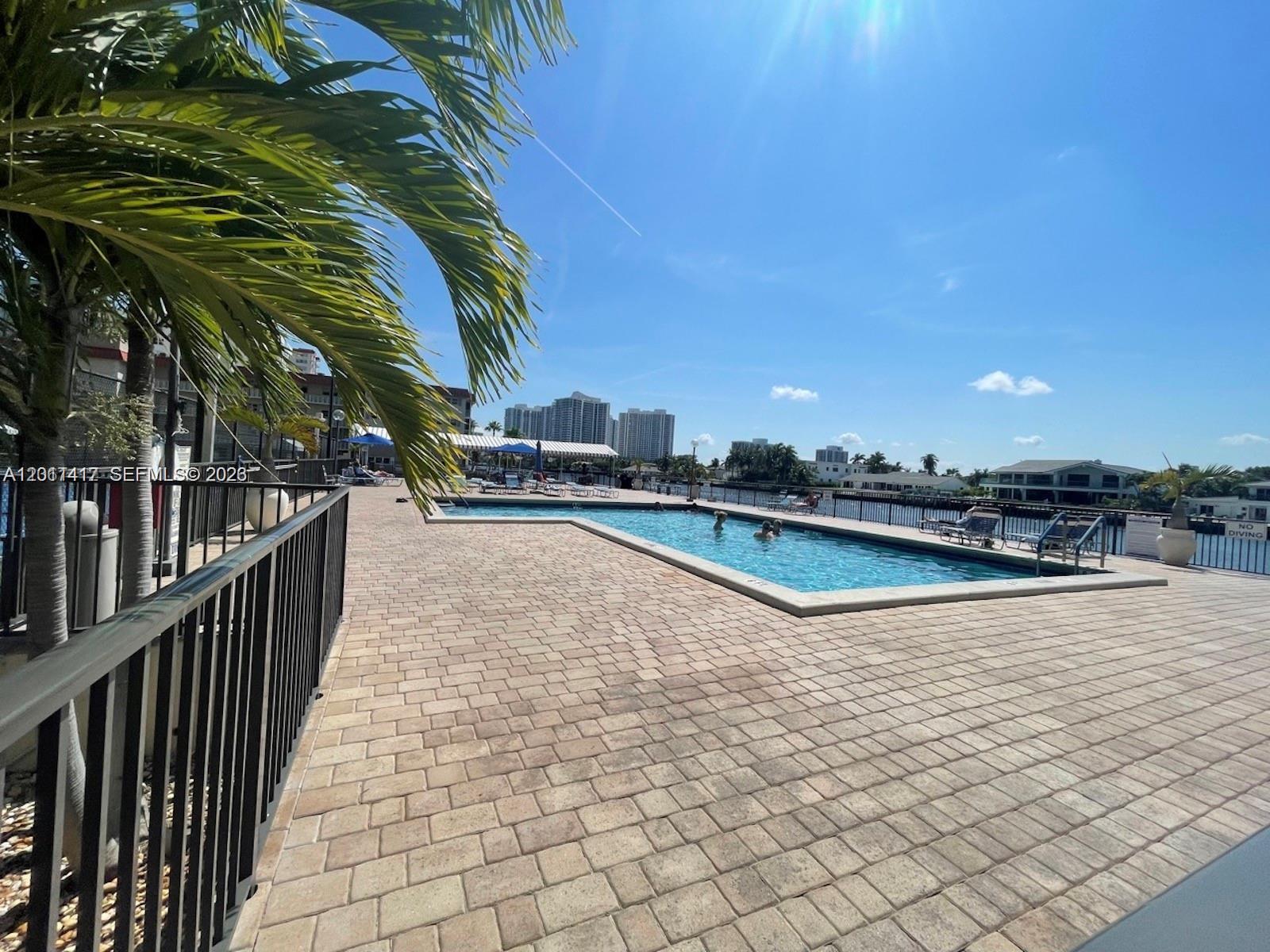 An outdoor swimming pool with a paved deck and palm trees overlooks a waterway — 2049 S Ocean Dr # 1504, Hallandale Beach FL 33009, HALLANDALE BEACH, FL