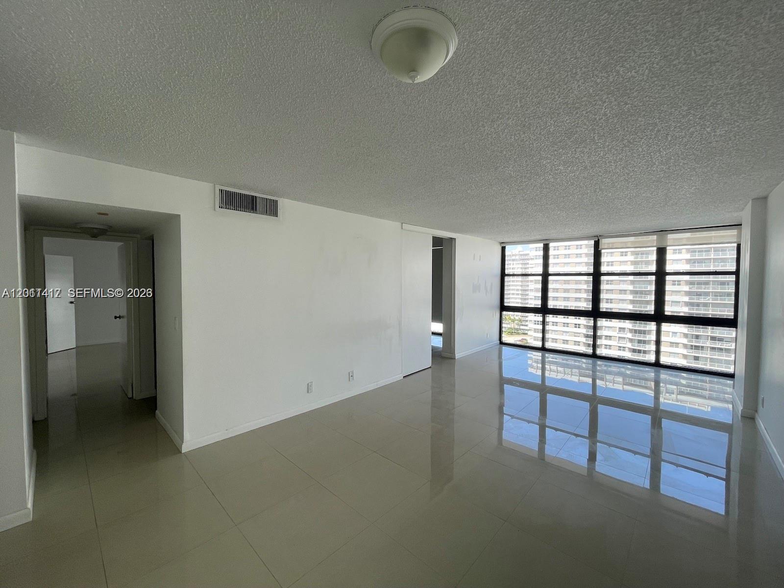 An empty living room features white walls, large floor tiles, and a wall of windows — 2049 S Ocean Dr # 1504, Hallandale Beach FL 33009, HALLANDALE BEACH, FL