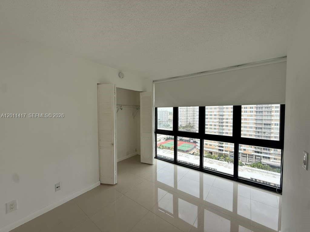A bedroom with white walls, tile flooring, a closet, and floor-to-ceiling windows overlooking buildings — 2049 S Ocean Dr # 1504, Hallandale Beach FL 33009, HALLANDALE BEACH, FL