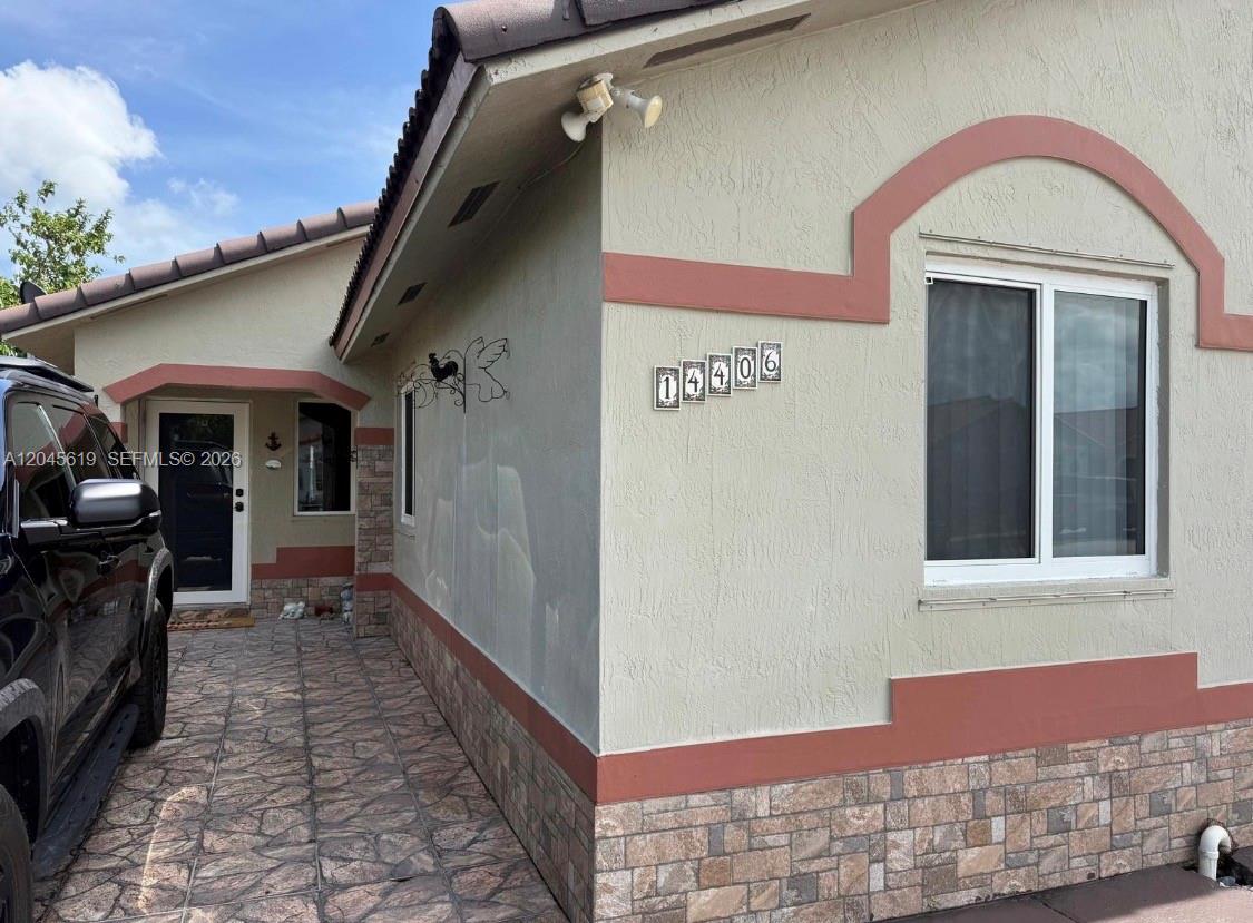 The exterior of a house features a stone-veneer base, stucco walls, and a tiled walkway — 14406 SW 179th Ln, Miami FL 33177, MIAMI, FL