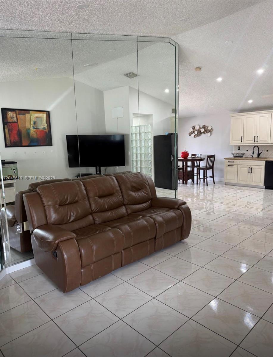 A living room with a brown leather sofa, mirrored wall, and an adjacent kitchen — 14406 SW 179th Ln, Miami FL 33177, MIAMI, FL