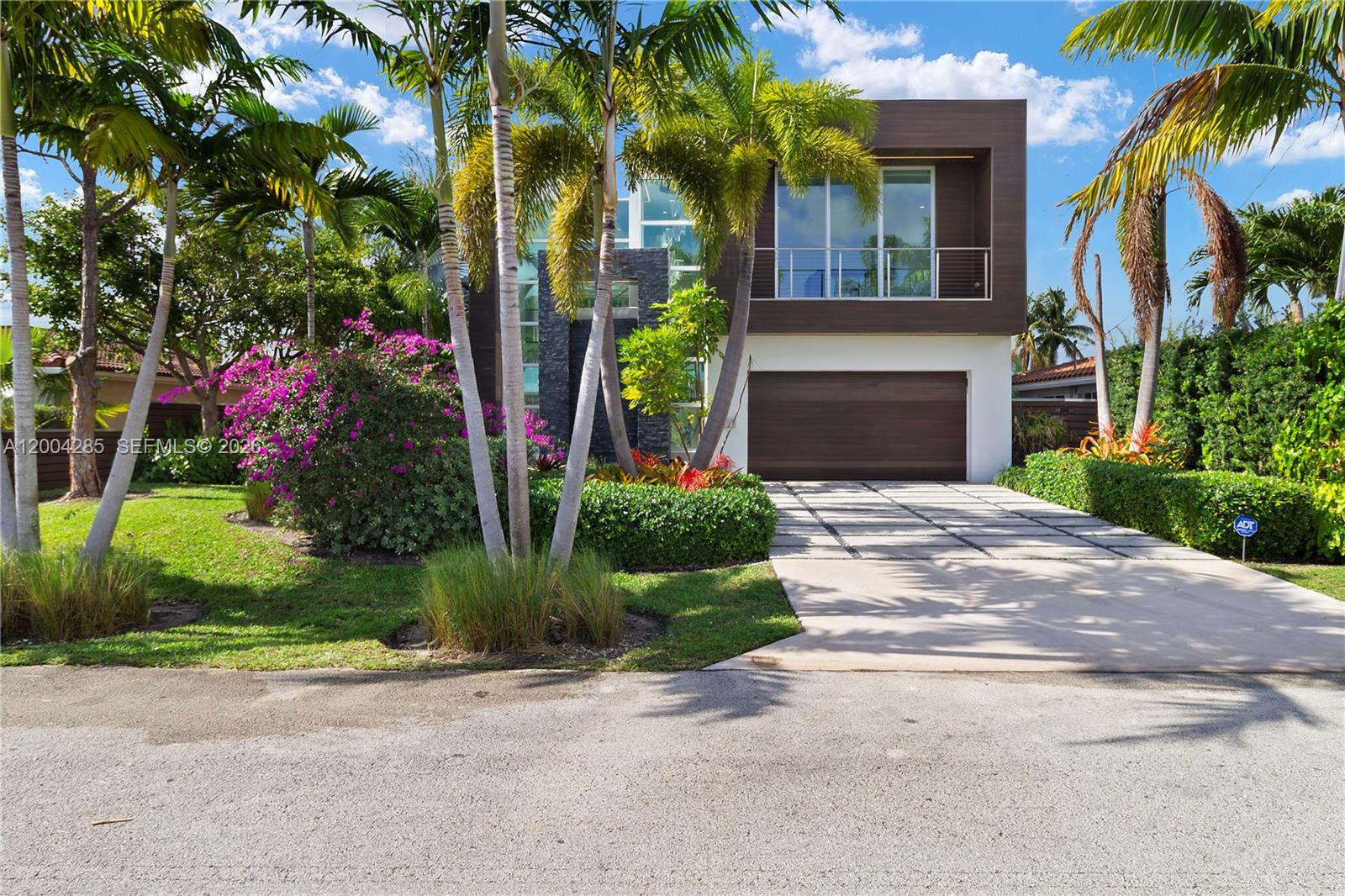 A modern two-story house features a wooden garage door, a balcony, and lush tropical landscaping — 2217 NE 17th Ter, Wilton Manors FL 33305, WILTON MANORS, FL