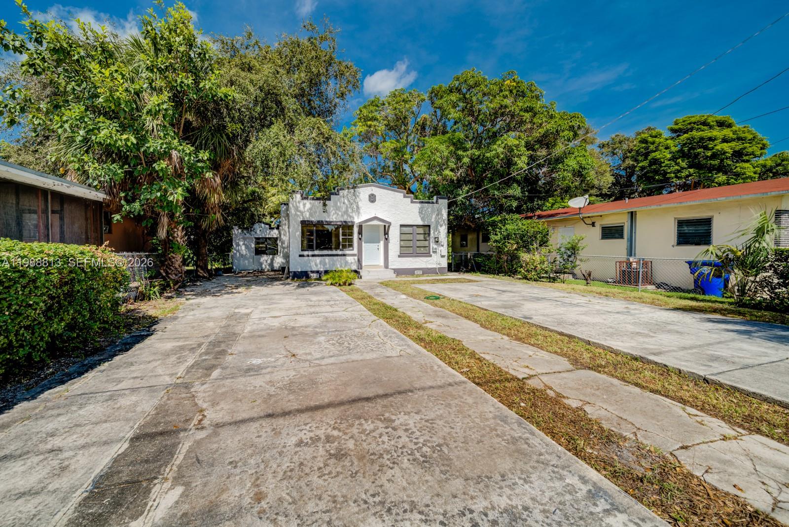 A white, single-story house with a flat roof features a concrete driveway and mature trees — 829 NW 56th St, Miami FL 33127, MIAMI, FL