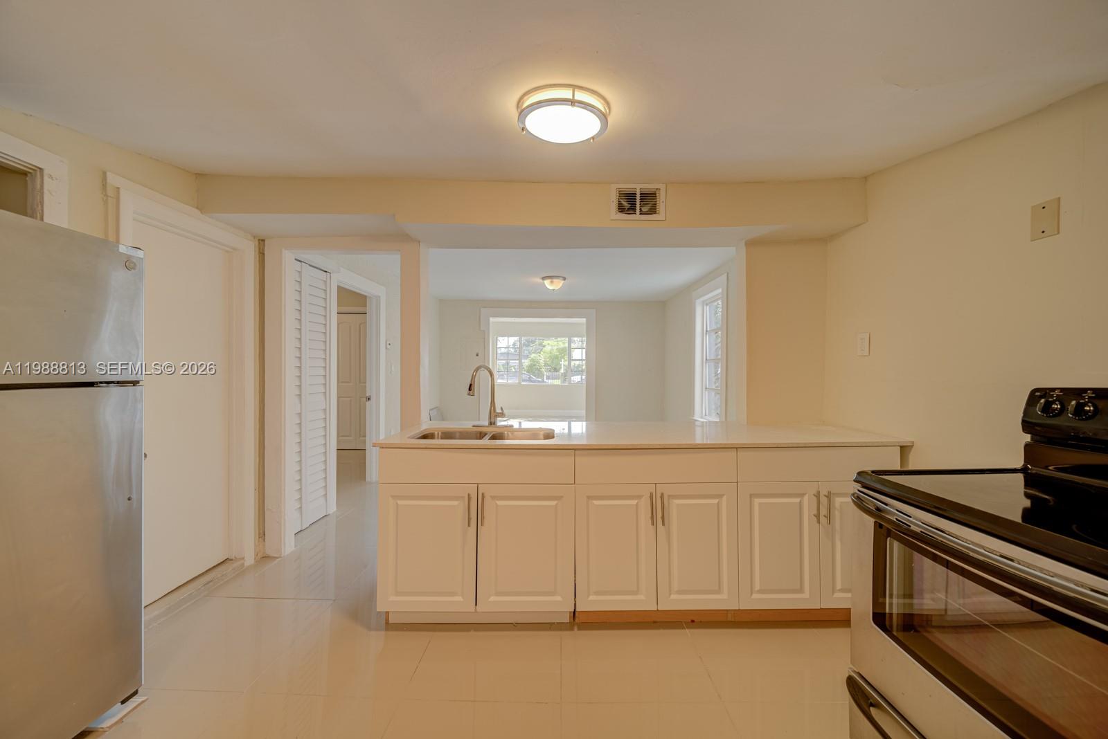 A kitchen features white cabinets, a stainless steel sink, and a view into another room — 829 NW 56th St, Miami FL 33127, MIAMI, FL