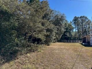 A vacant, grassy lot is bordered by dense trees and a white fence — 7991 N TINY LILY DRIVE, CITRUS SPRINGS, FL