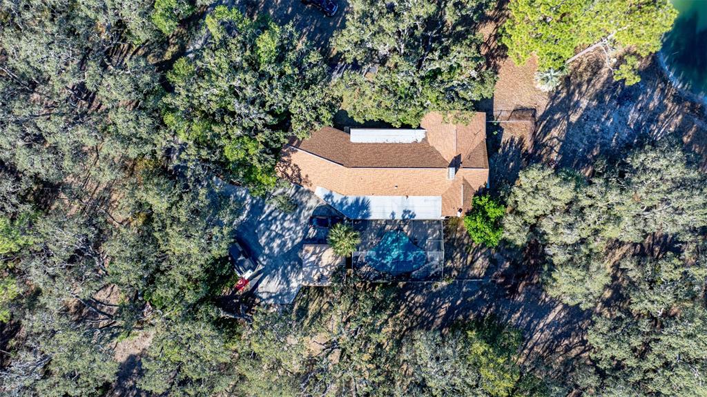 An aerial view shows a house with a pool enclosure surrounded by dense trees — 13615 TYRONE STREET, HUDSON, FL