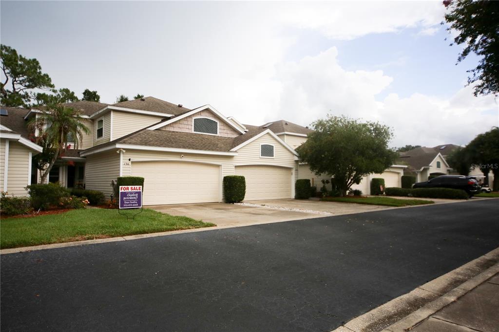 A two-story townhouse with beige siding and two attached garages sits along a paved road — 136 BAYTREE BOULEVARD, TAVARES, FL