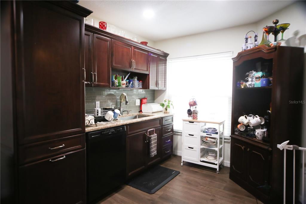 A kitchen features dark wood cabinets, a black dishwasher, and a white rolling storage cart — 136 BAYTREE BOULEVARD, TAVARES, FL