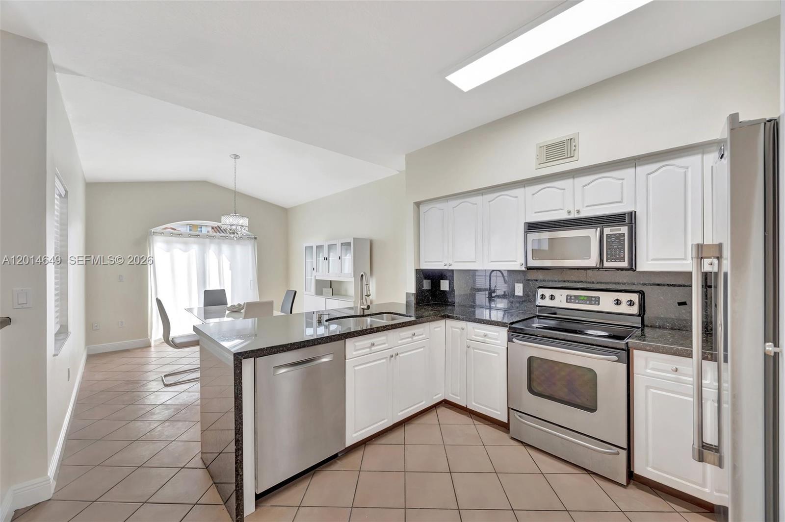 A kitchen with white cabinets, stainless steel appliances, and dark countertops opens to a dining area — 10110 SW 154th Cir Ct # 1, Miami FL 33196, MIAMI, FL