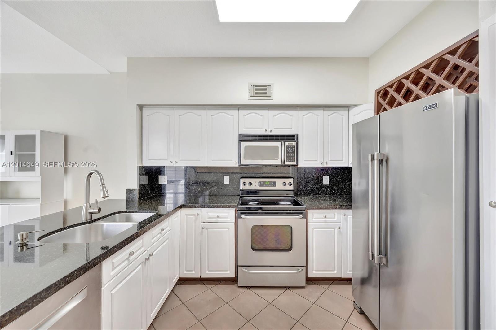A kitchen features white cabinets, dark granite countertops, stainless steel appliances, and tile flooring — 10110 SW 154th Cir Ct # 1, Miami FL 33196, MIAMI, FL