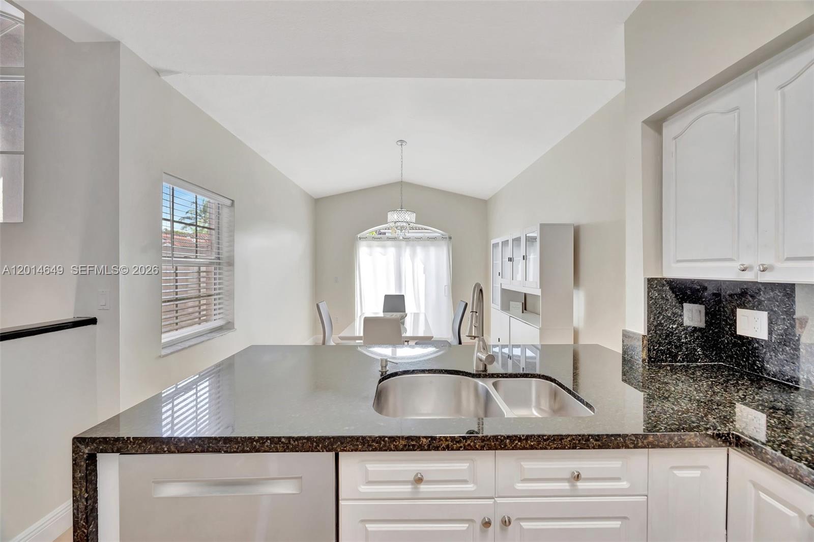 A kitchen with dark granite countertops and white cabinets overlooks a bright dining area — 10110 SW 154th Cir Ct # 1, Miami FL 33196, MIAMI, FL