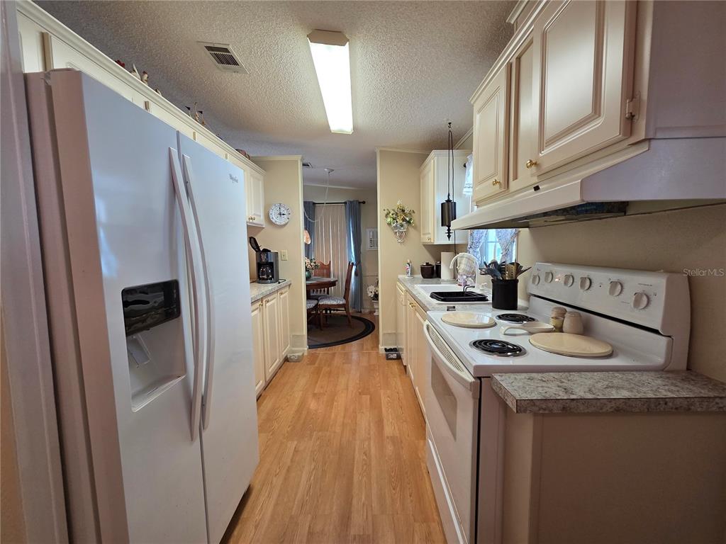 A galley-style kitchen features white appliances, light-colored cabinetry, and wood-look flooring — 4157 71ST LANE N UNIT 14, ST PETERSBURG, FL
