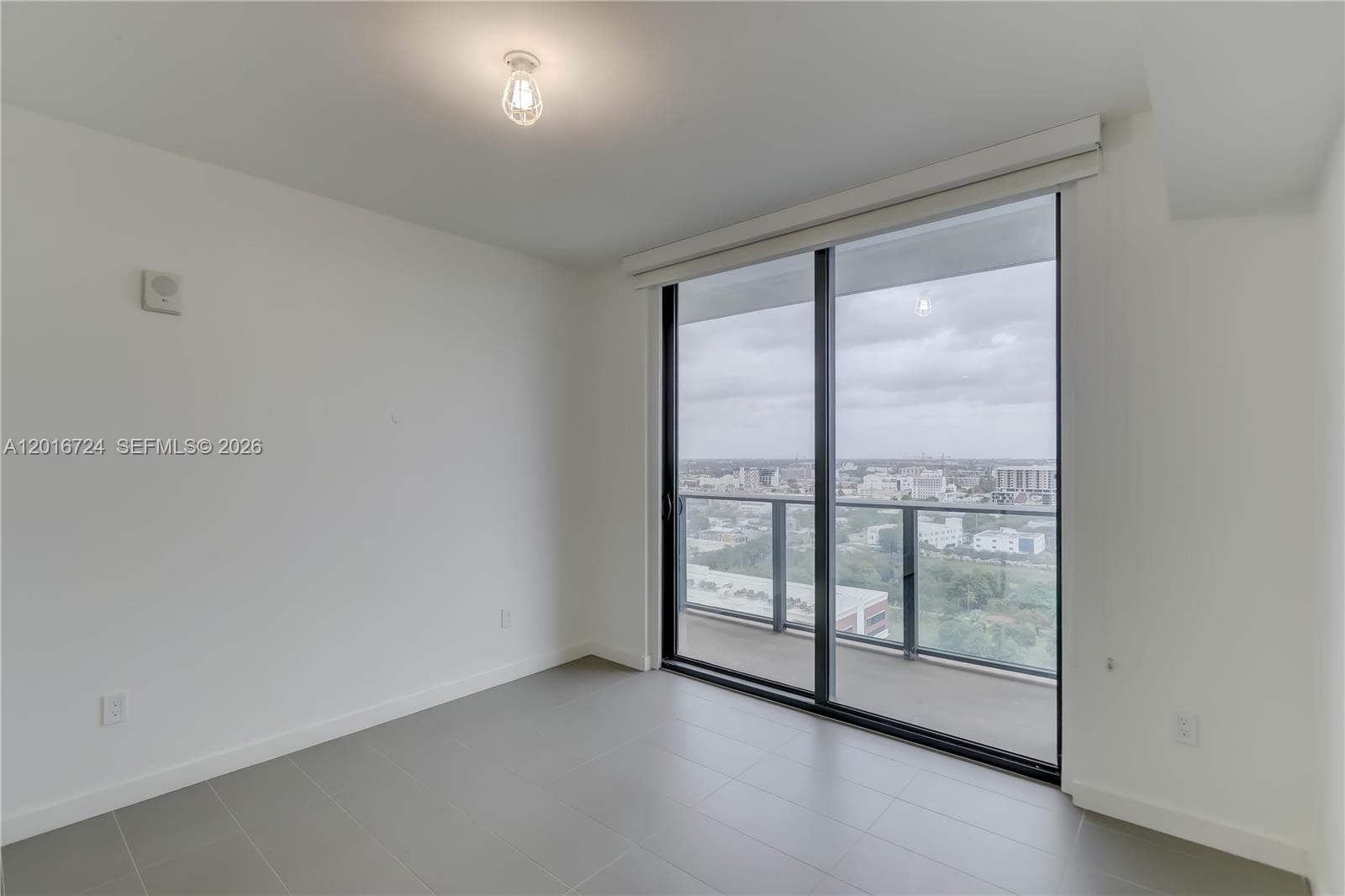 A minimalist room features gray tile flooring, white walls, and a large sliding glass door — 1600 NE 1st Ave # 1918, Miami FL 33132, MIAMI, FL