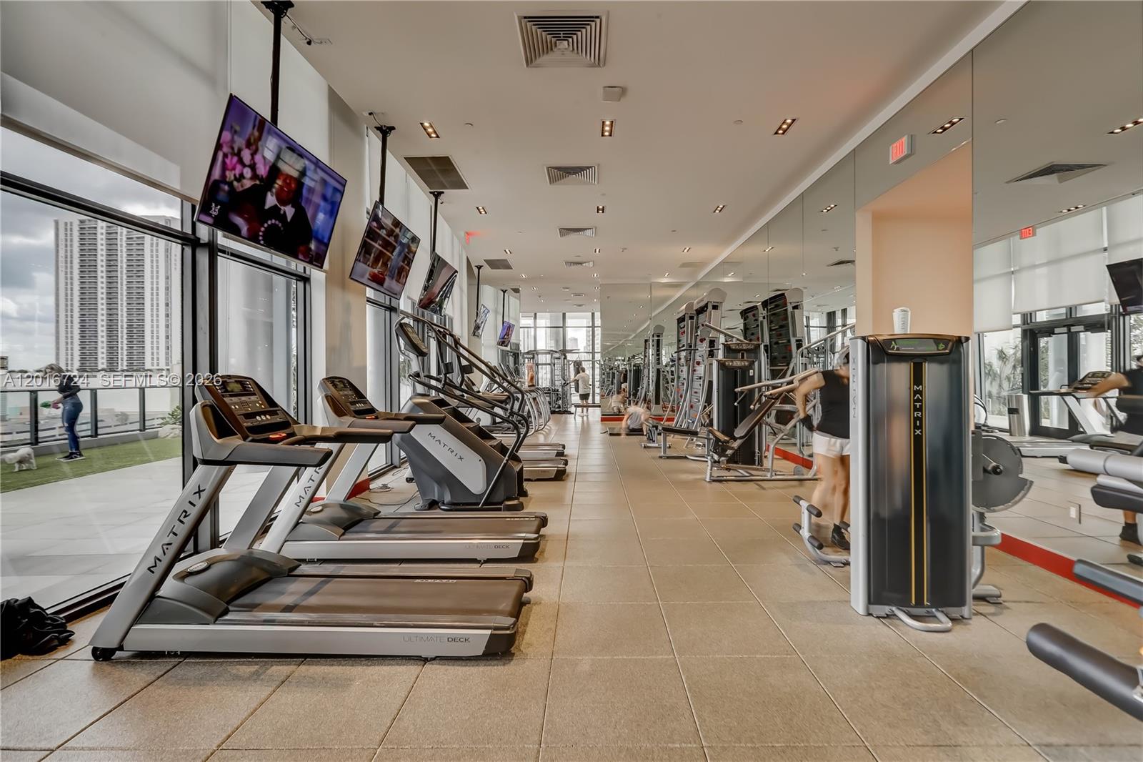 A modern gym features rows of Matrix treadmills, weight machines, mirrored walls, and floor-to-ceiling windows — 1600 NE 1st Ave # 1918, Miami FL 33132, MIAMI, FL